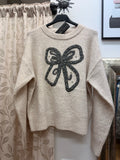 Jersey de mujer color crudo con gran lazo gris de punto y pedrería