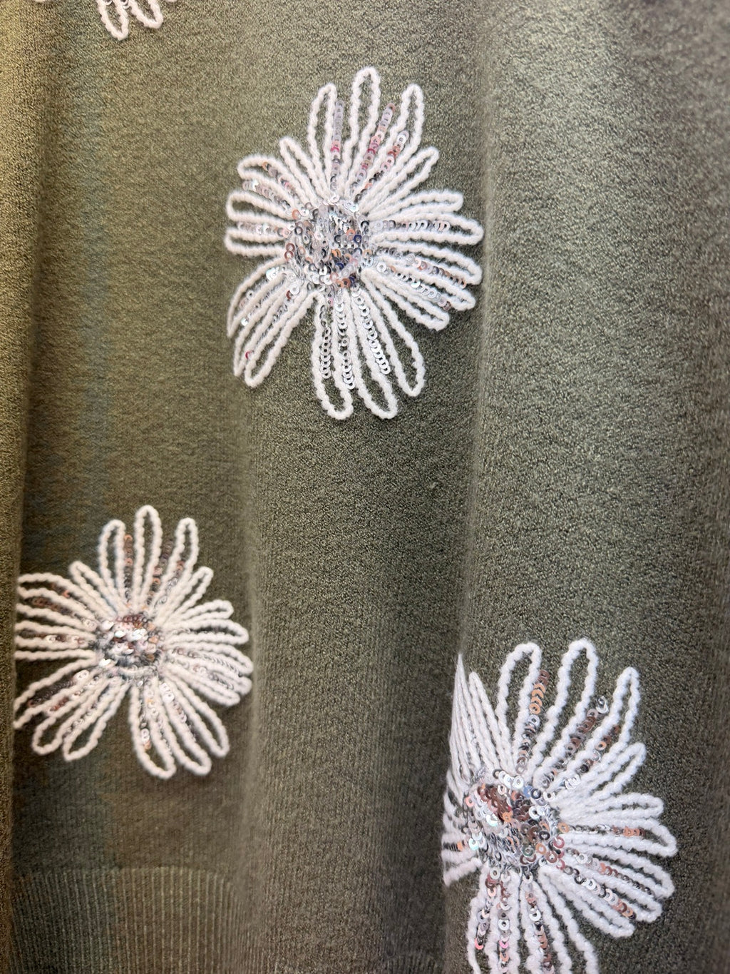 Detalle de flores bordadas con lentejuelas del jersey verde de mujer