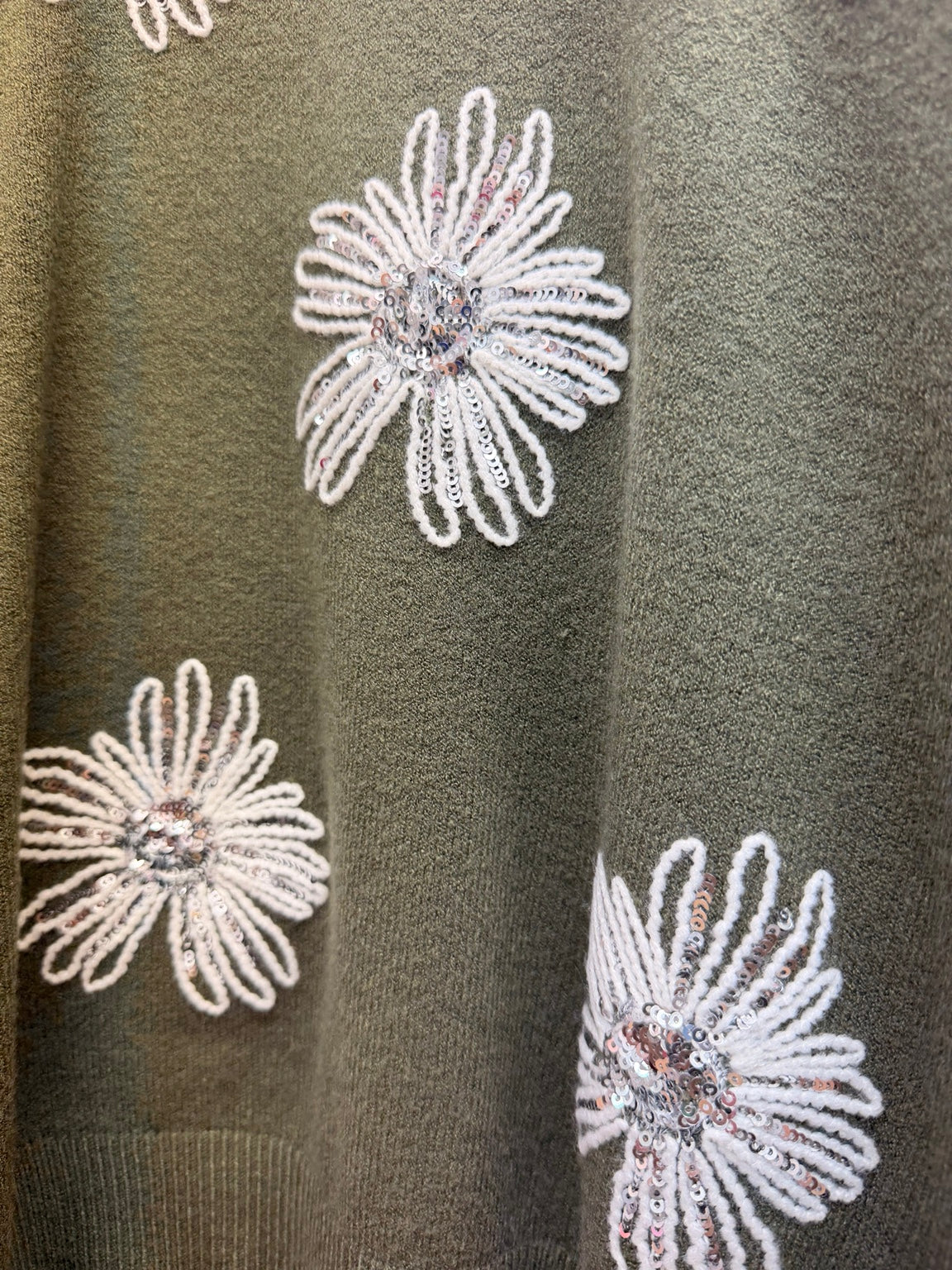 Detalle de flores bordadas con lentejuelas del jersey verde de mujer