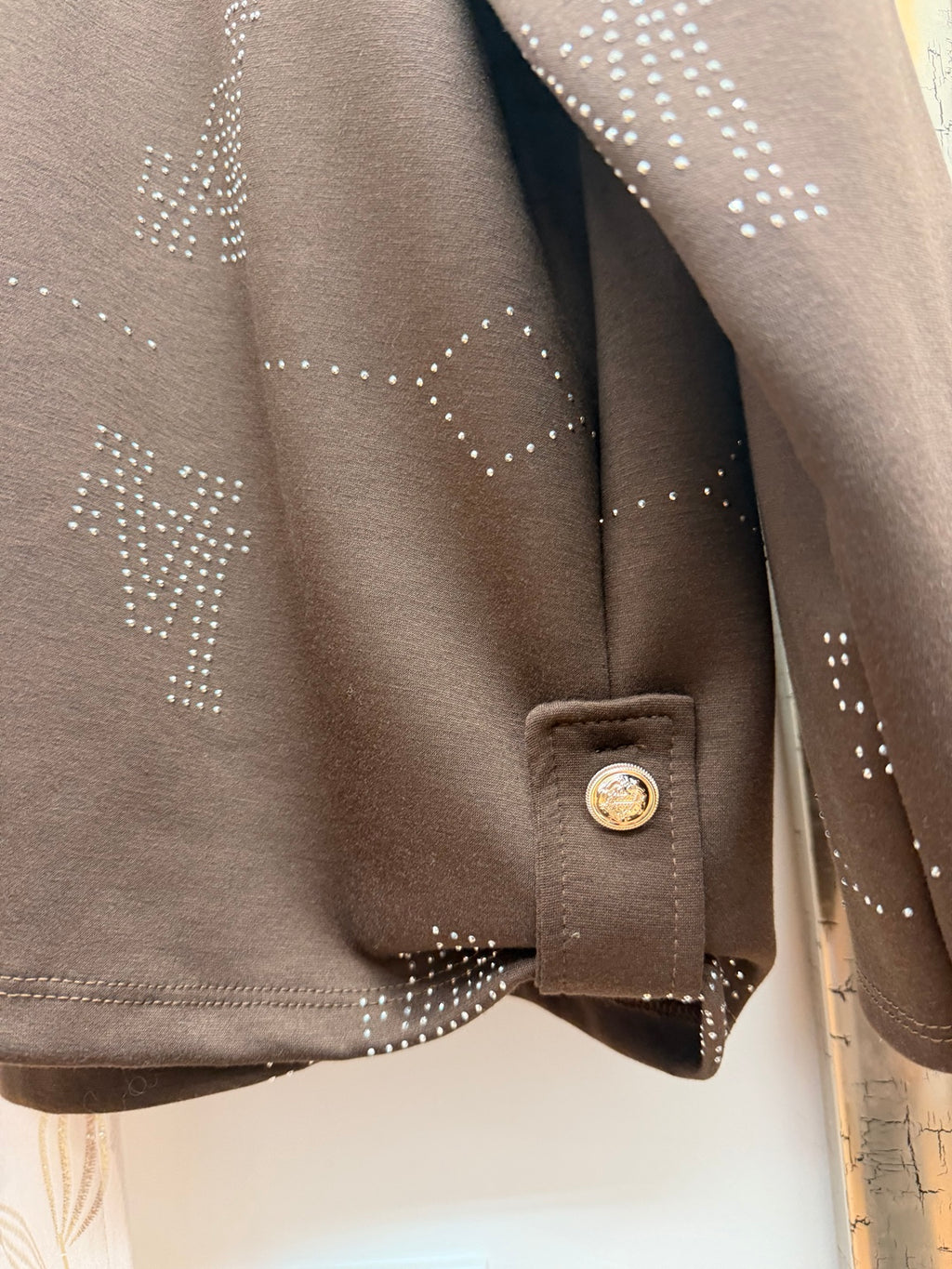 Detalle del bajo con botón decorativo de la sudadera marrón con strass