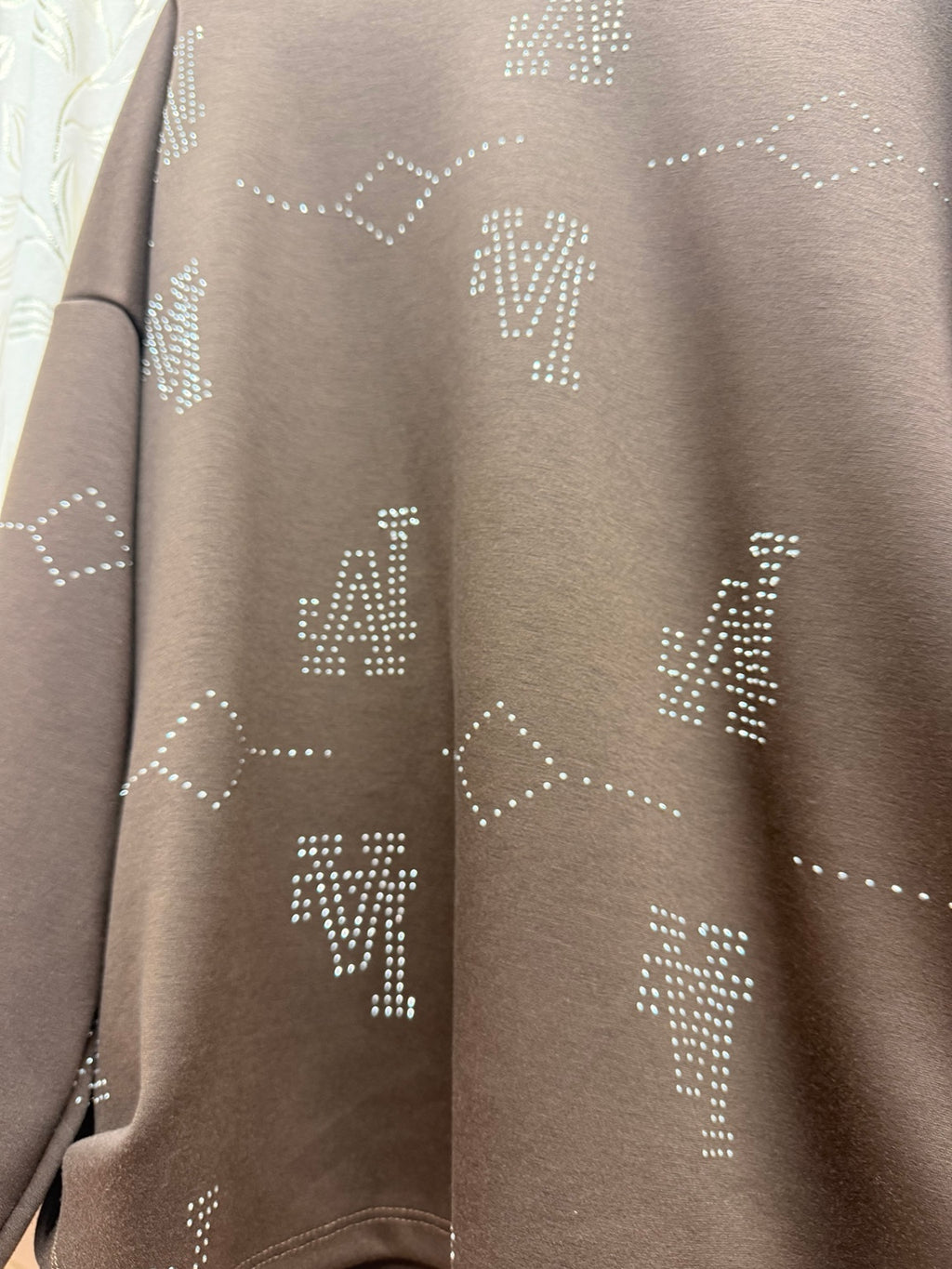 Detalle de los motivos geométricos de strass de la sudadera marrón de mujer