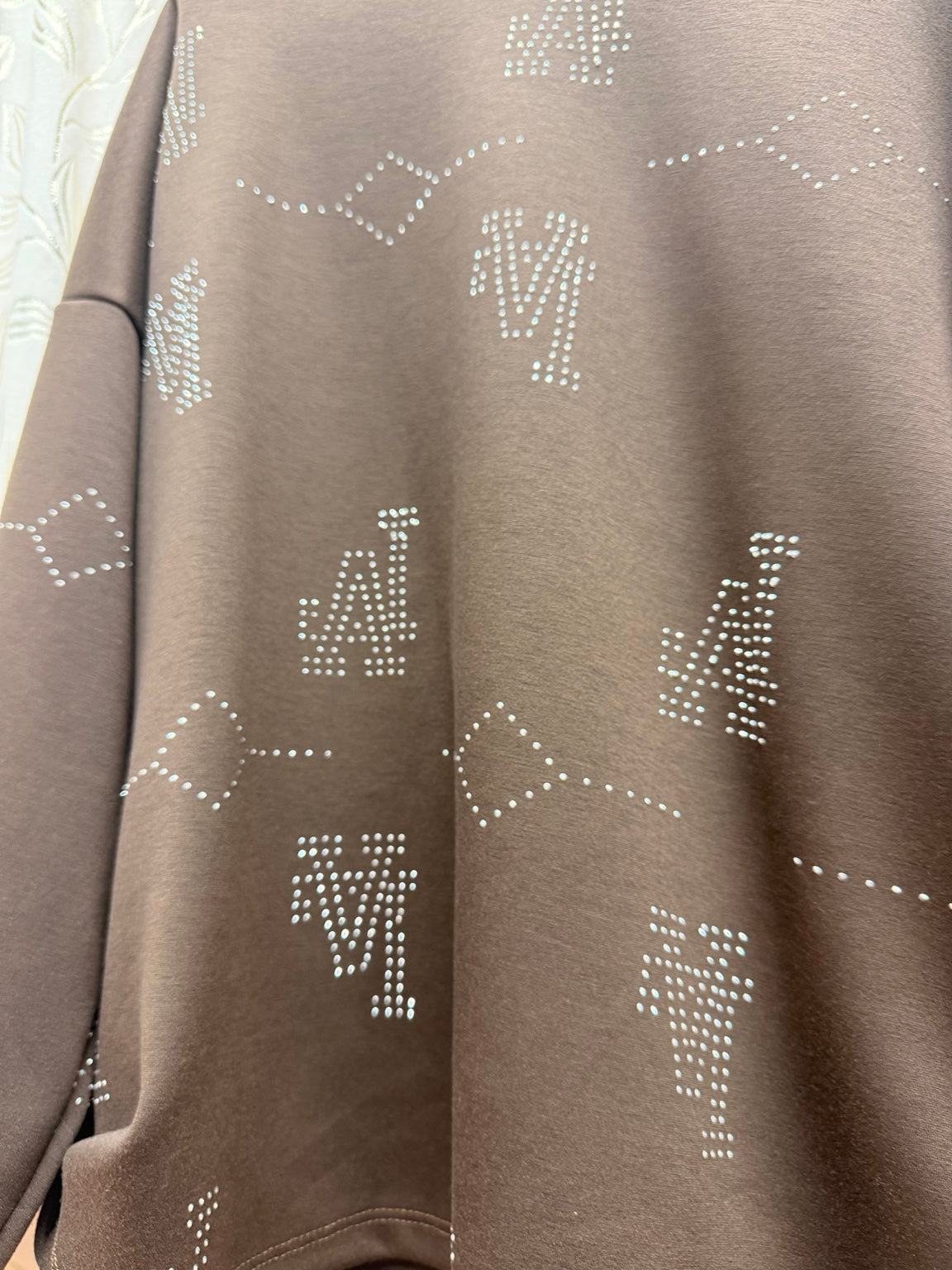 Detalle de los motivos geométricos de strass de la sudadera marrón de mujer